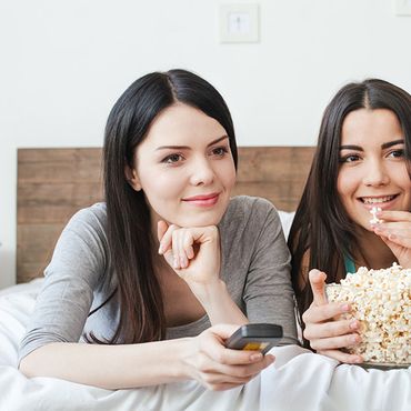2 junge Frauen mit Popcorn vor dem Fernseher