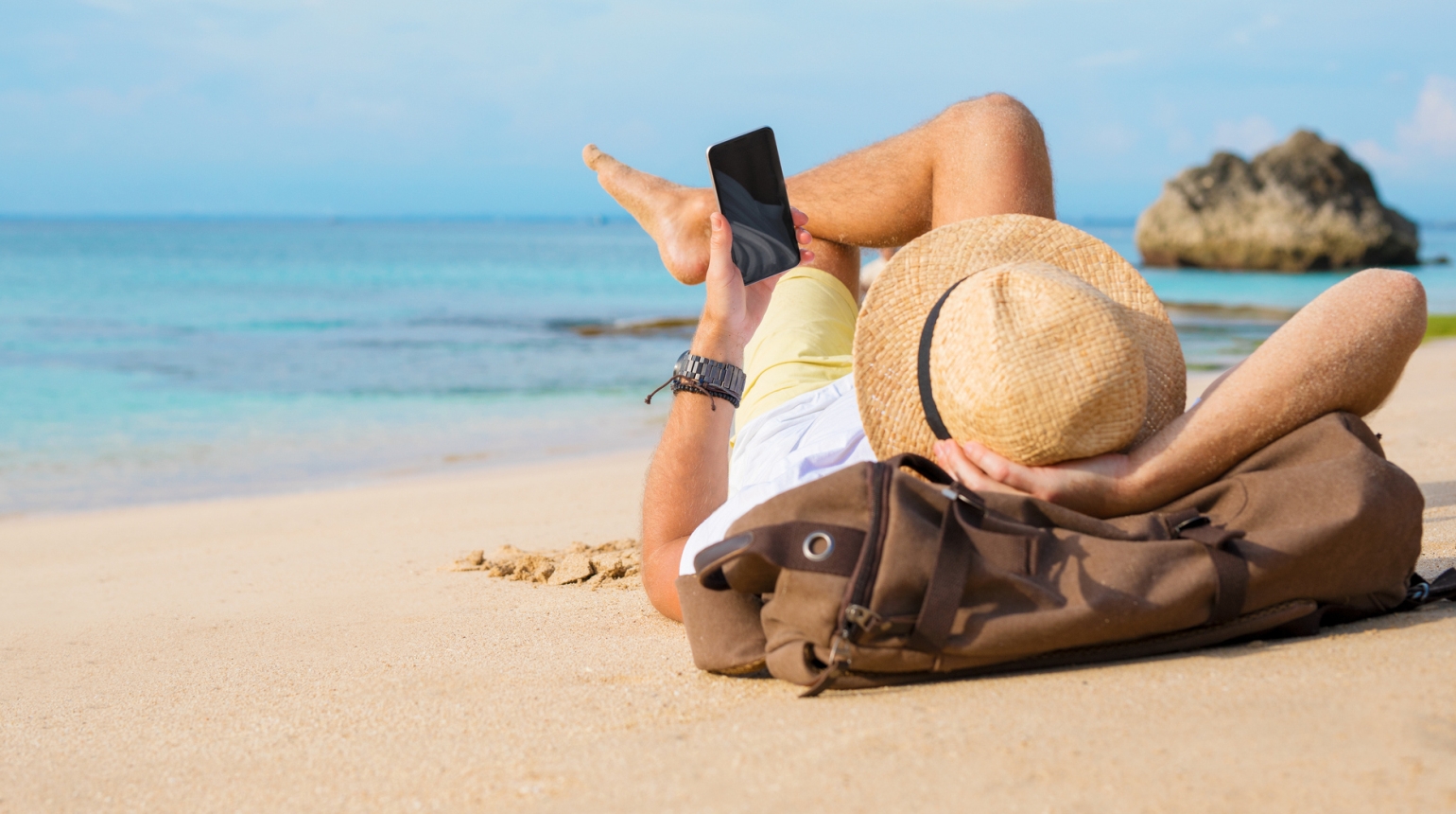 Mann liegt gemütlich am Sandstrand während er auf sein Smartphone schaut. I