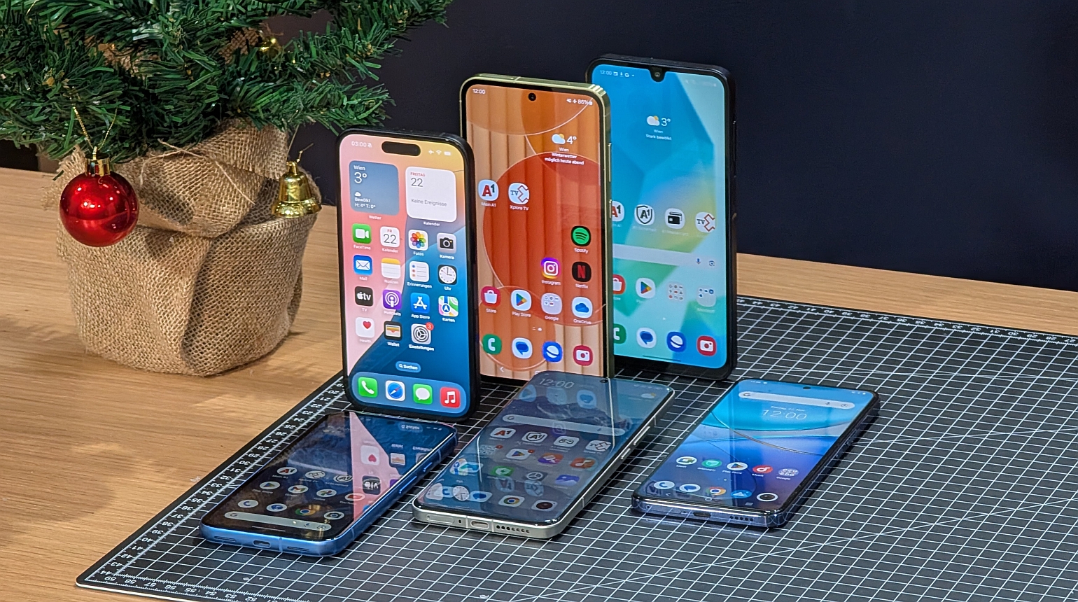 6 Smartphones neben Weihnachtsbaum auf schwarzem Hintergrund